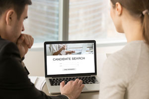 image of two people looking at a laptop screen.  Candidate search on the screen